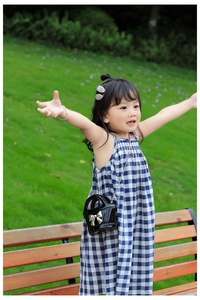 Detail of girls' blue gingham dress paired with a black bow crossbody bag in a park