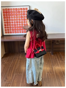 Detail of children's black leather crossbody bag with red handle and chain strap on back