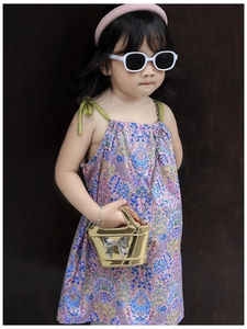 Close-up of metallic golden kids handbag with silver bow and pink floral summer dress