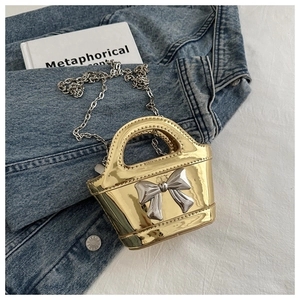 Detail of a shiny gold metallic mini bag with a silver bow and metal chain strap
