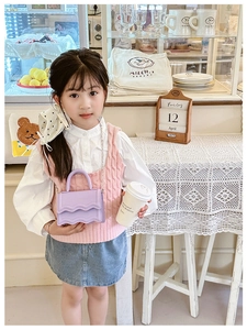 Detail of a purple mini girls bag with wavy flap design and metal chain strap in a cafe
