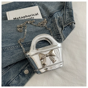 Detail of silver metallic mini bag with bow decoration and chain strap on denim fabric