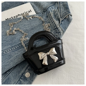 Detail view of a black glossy patent leather girls' bag with a silver bow and chain strap