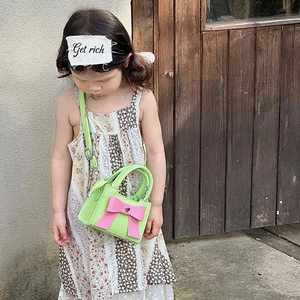 Détail d'un sac bandoulière vert pour enfant avec grand nœud rose et breloque cœur argentée