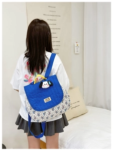 Close-up of blue quilted flap backpack with floral pattern and cute dog pendant