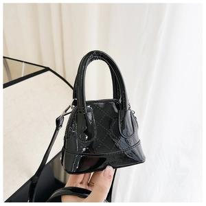 Détail du sac coquille en cuir verni noir avec texture matelassée et logo de la marque