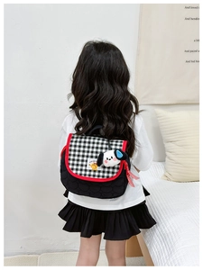 Detail of children's checkered backpack featuring a cute puppy plush charm and red trim