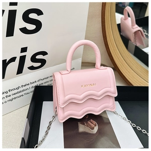 Pink mini crossbody bag with wavy edge flap and gold chain strap on minimalist display