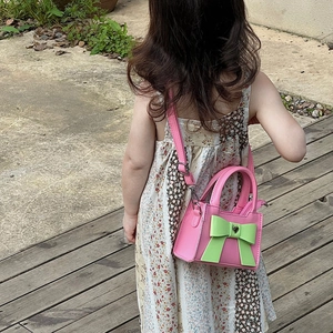 Fillette portant un sac rose à bandoulière avec grand nœud vert et fermoir cœur argenté
