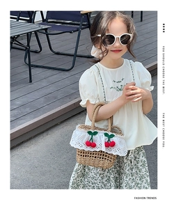 Detail of straw woven handbag with white lace trim and decorative red crochet cherries