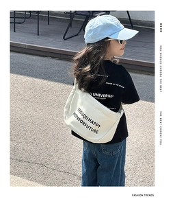 Détail d'un sac à bandoulière en toile blanche avec texte noir et sangle réglable