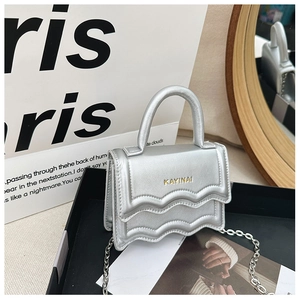 Close-up of silver mini bag featuring tiered wave design and golden letter logo detail