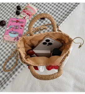 Detail view of the spacious inner lining and strawberry charm on the straw handbag
