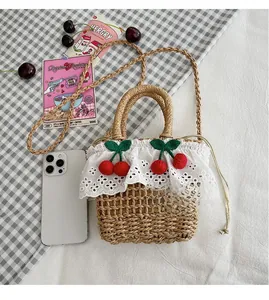 Detail view of woven straw handbag featuring lace trim, cherry charms, and phone size scale