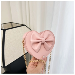 Détail du sac bandoulière rose en forme de cœur avec grand nœud et chaîne dorée