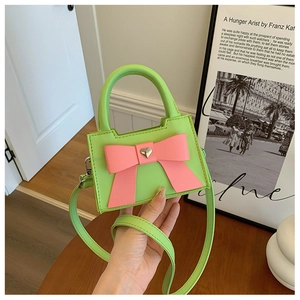 Détail montrant une main tenant un mini sac vert avec un nœud rose et boucle cœur