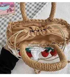 Detail view of woven straw handbag featuring a drawstring closure and cherry decorations