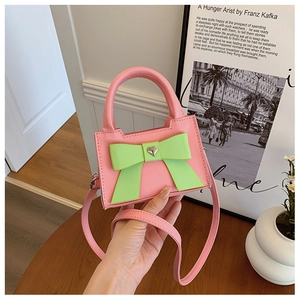 Détail du mini sac rose avec nœud vert et breloque cœur sur une table en bois