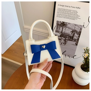 Détail du mini sac à main blanc avec nœud marine et breloque cœur doré en main