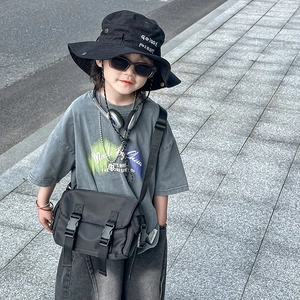 Minimalist black kids messenger bag in durable nylon with buckle straps on stone steps