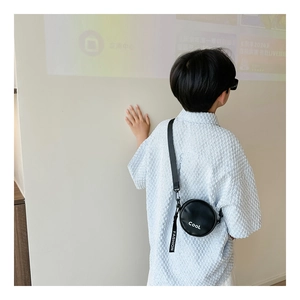 Detailed view of black round boys' crossbody bag with white Cool print and fashion strap