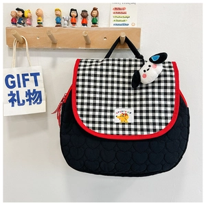 Detail of black quilted backpack featuring checkered flap and cute plush dog pendant