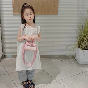 Fillette portant un mini sac bandoulière rose avec poignée dans un décor minimaliste