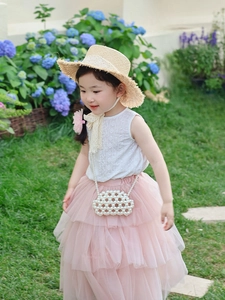 Detail of girls' white pearl cloud bag and straw hat in a scenic garden setting