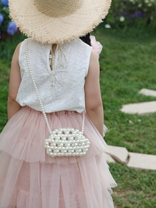 Outdoor shot of a child wearing a white pearl woven crossbody bag with a lace top