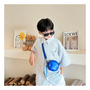Detail of round blue leather kids crossbody bag with white COOL lettering on blue shirt
