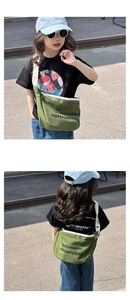 Vue de l'enfant portant le sac bandoulière en toile verte avec imprimé de lettres