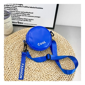 Detail view of round blue crossbody bag with white COOL lettering on a woven mat