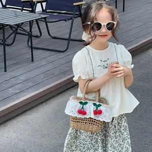 Detail of child straw handbag featuring white lace trim and red crochet cherries