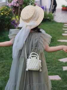 Détail d'un sac panier en perles pour fille avec robe verte à volants et chapeau de paille
