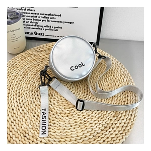 Detail of silver circular mini bag featuring black COOL lettering and nylon strap