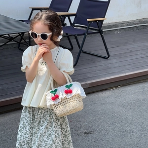 Detail of straw woven handbag with cherry accents and white lace on outdoor terrace
