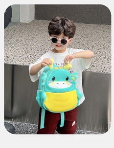 Detail of cute green cartoon dragon backpack with 3D horns on a young boy model