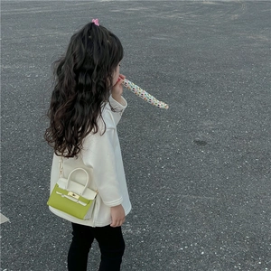 Fillette portant un mini sac bandoulière vert et blanc stylé sur un sol extérieur