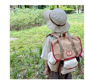 Rear view of kid wearing a beige and white color-block backpack in an outdoor park setting