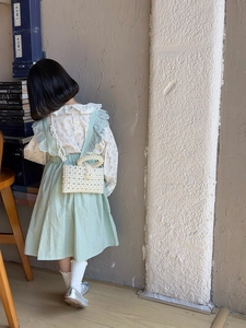 Detail of child wearing a beaded pearl crossbody bag with a green ruffled summer dress