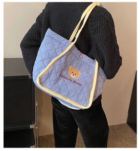 Detail of blue quilted tote bag with cute bear embroidery and yellow handle accents
