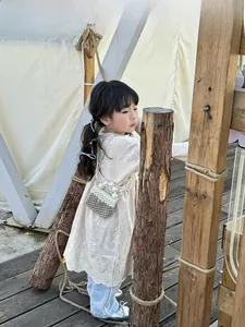 Detail of child wearing a silver and white pearl woven crossbody bag on wooden deck