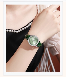 Detail of green leather watch band and rhinestone bezel with date display on dial