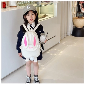 Detail view of white toddler backpack with pink rabbit ears and pompom decor on small bag