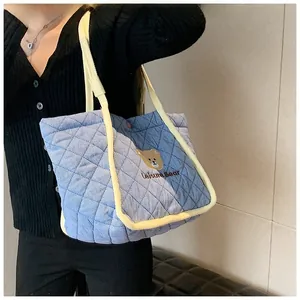 Detail of blue quilted tote bag with brown bear embroidery and yellow contrast straps