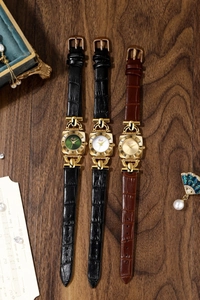 Three vintage square quartz watches with leather straps and gold cases on wood