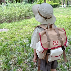 Kids outdoor canvas backpack with red contrast trim and adjustable straps on a grass field