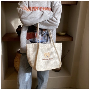 Close-up of cute brown bear embroidery and quilted texture on a beige canvas tote bag