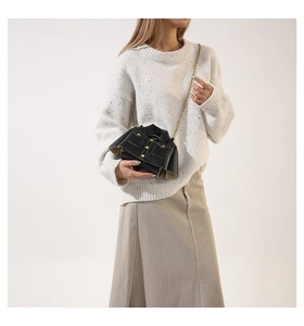 Close-up of black leather jacket-shaped crossbody bag with gold chain strap on model