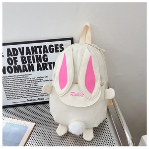 Detail of cream rabbit backpack with pink plush ears and white pom-pom tail on a metal chair